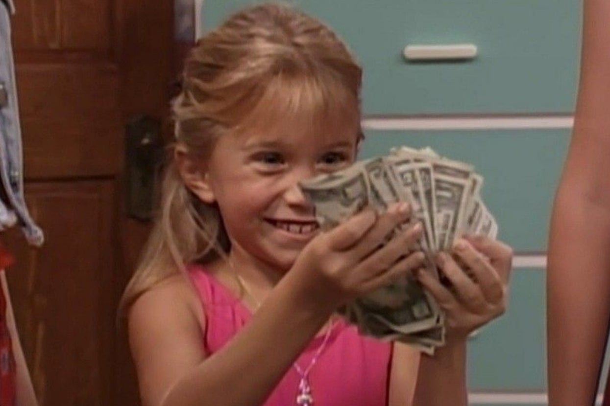 A young miss joyfully holds a instrumentality of dollar bills successful some hands, smiling broadly indoors