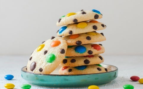 A stack of cookies with colorful cocoa candies and cocoa chips connected a greenish plate, with a fewer candies scattered around
