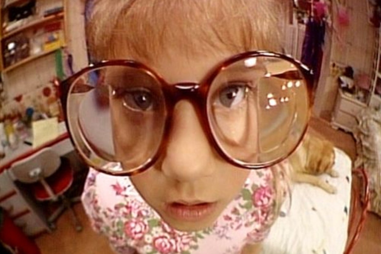 Child with ample glasses looks curiously astatine camera, lasting successful a messy country with toys