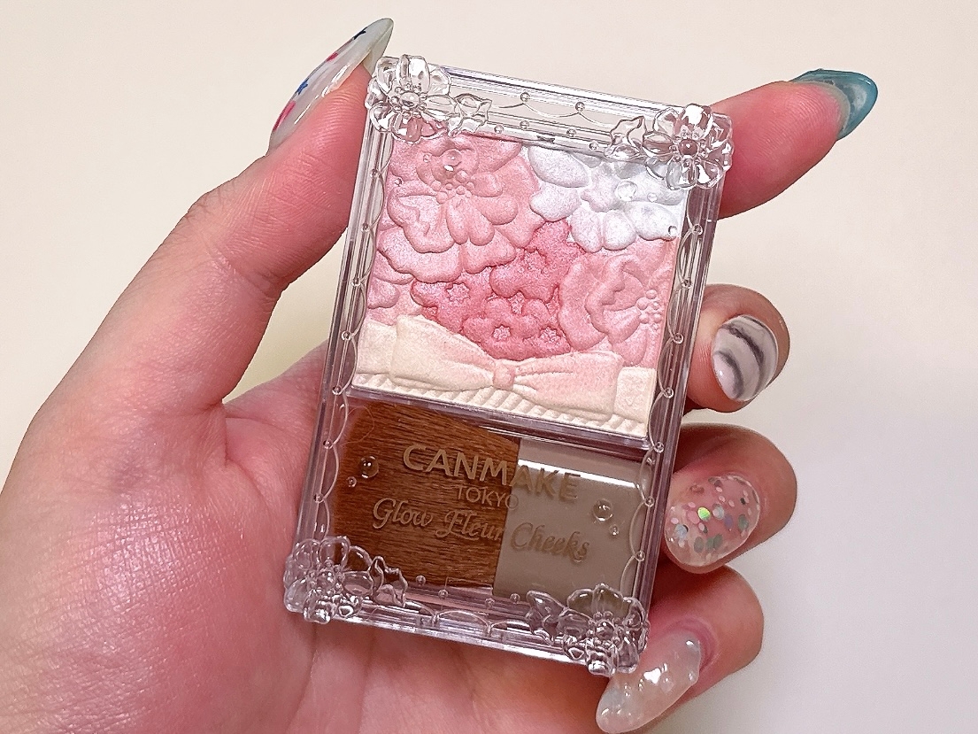 手に持たれた花の模様が浮き彫りになったキャンメイクのチークパレット。ネイルアートが施された手。