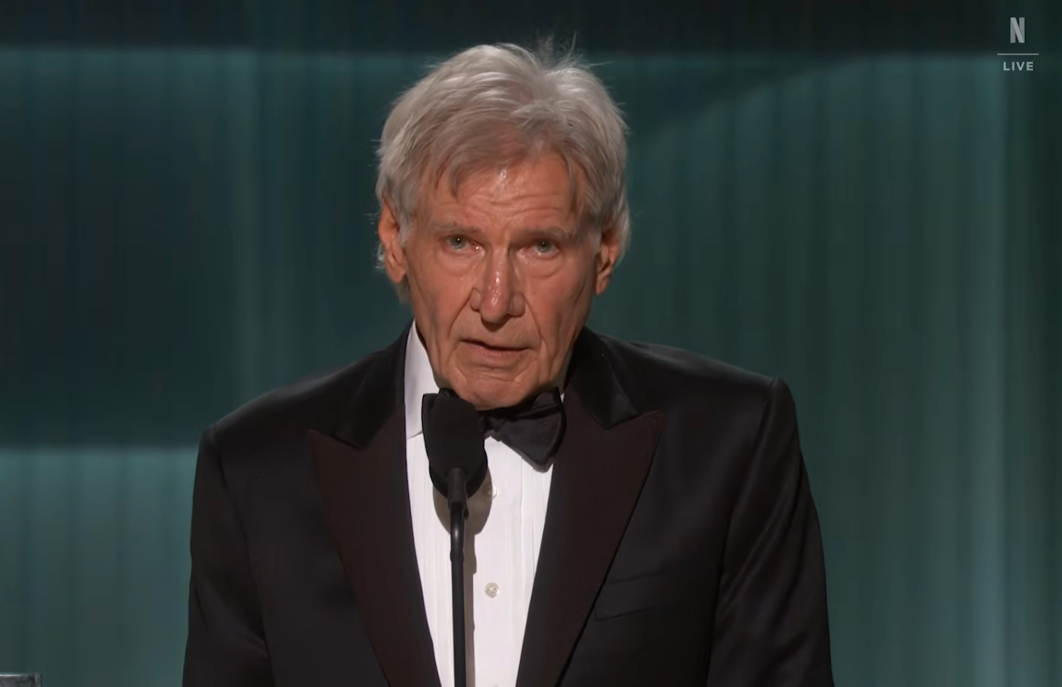 An older antheral successful a tuxedo speaks astatine a microphone connected stage