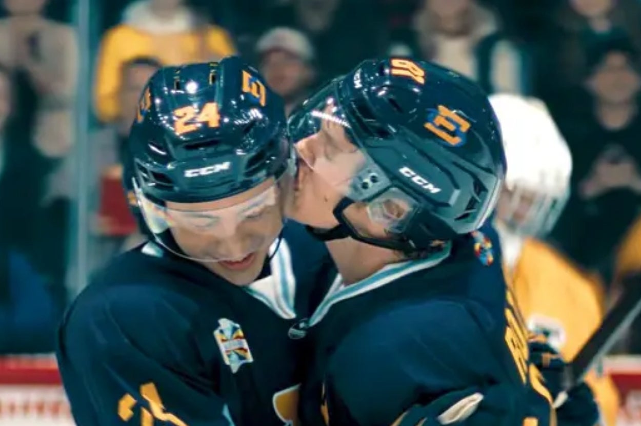 Two hockey players in team jerseys celebrate a goal on the ice, with one player joyfully kissing the other on the cheek
