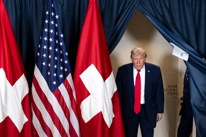 A person in a suit stands between U.S. and Swiss flags at the World Economic Forum entrance
