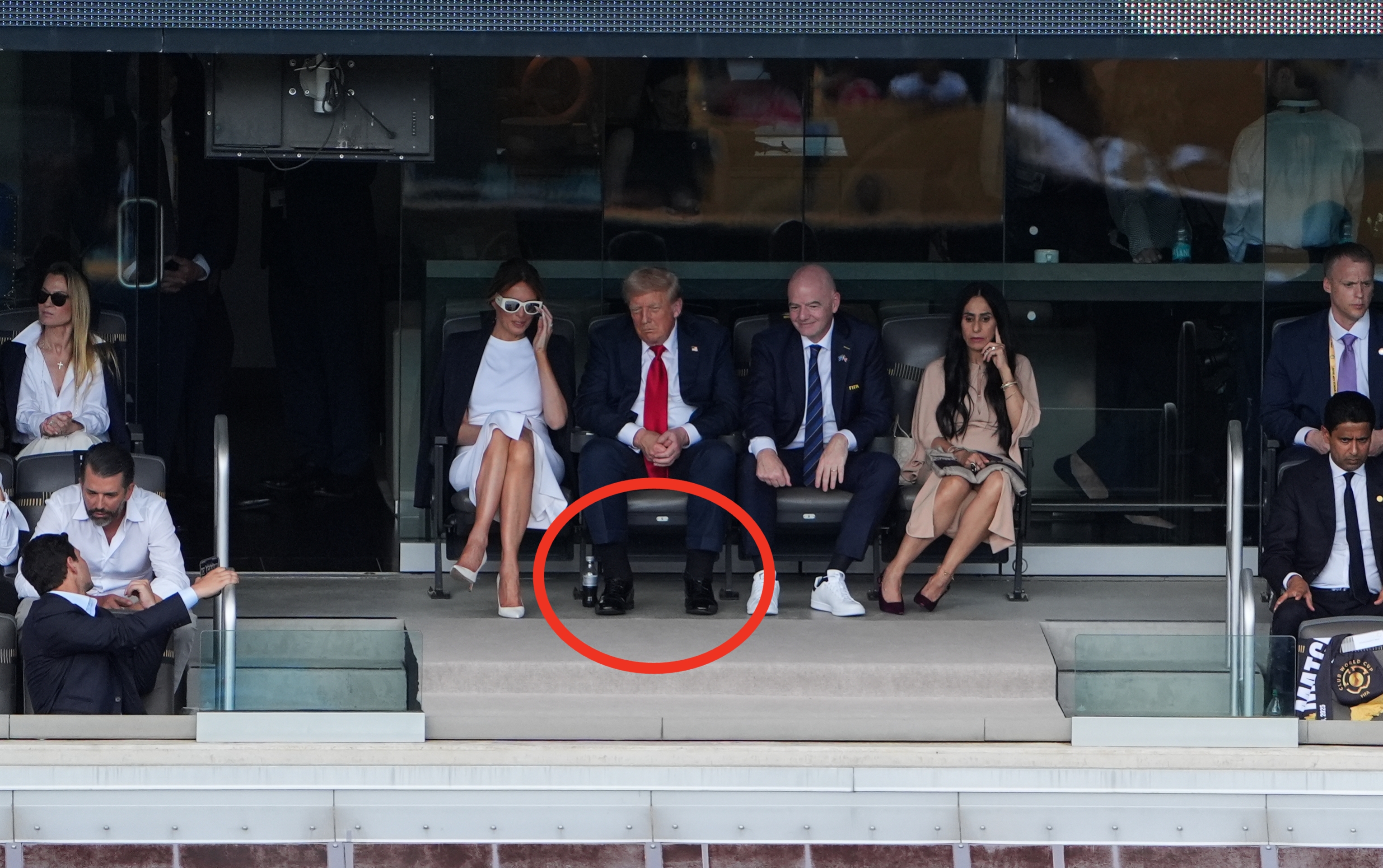 People seated in a stadium box, including a man in a suit and tie, watching the event below. Others are casually dressed or wearing formal attire