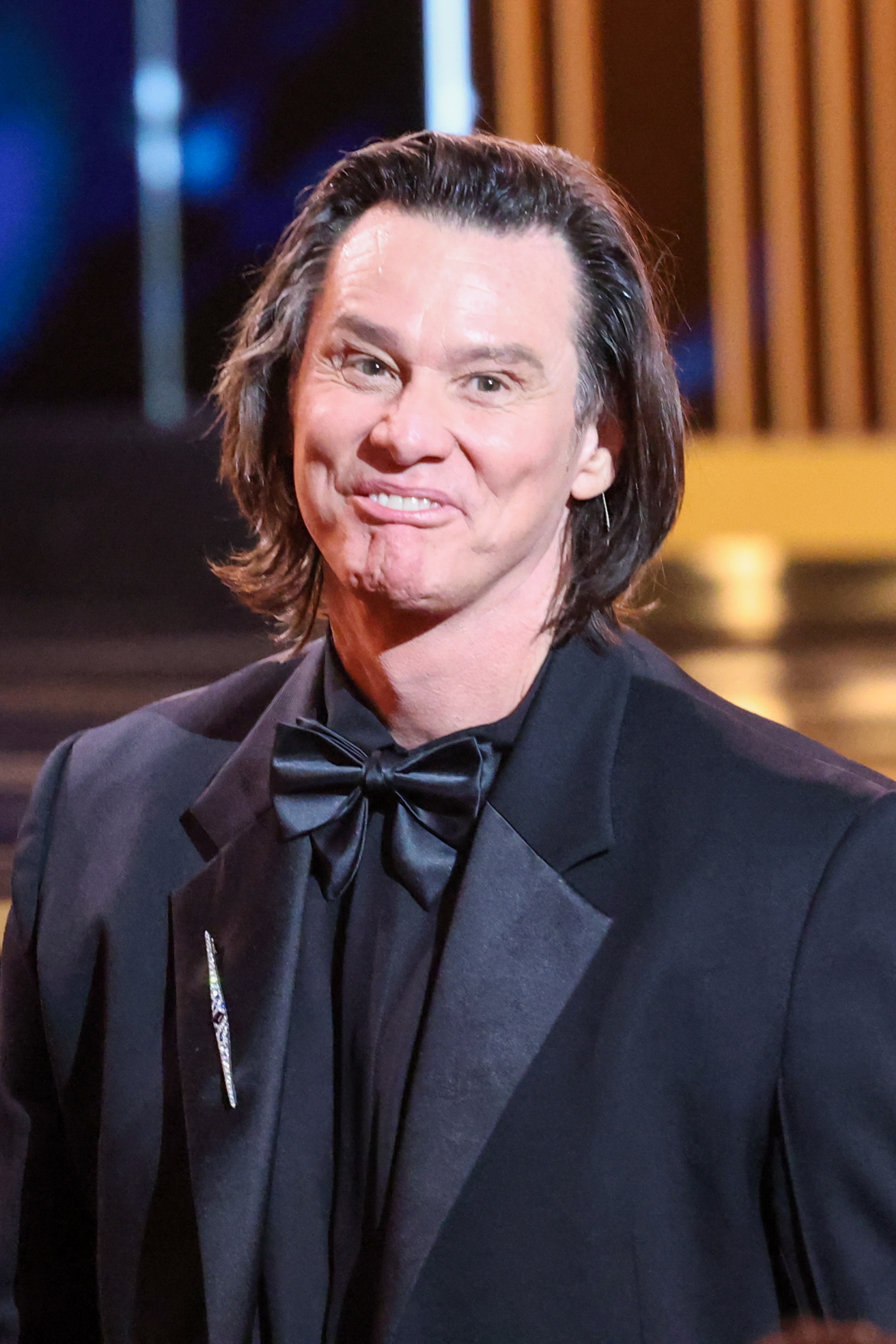 Person successful a ceremonial achromatic suit with a bow tie, smiling connected a signifier with lights successful the background