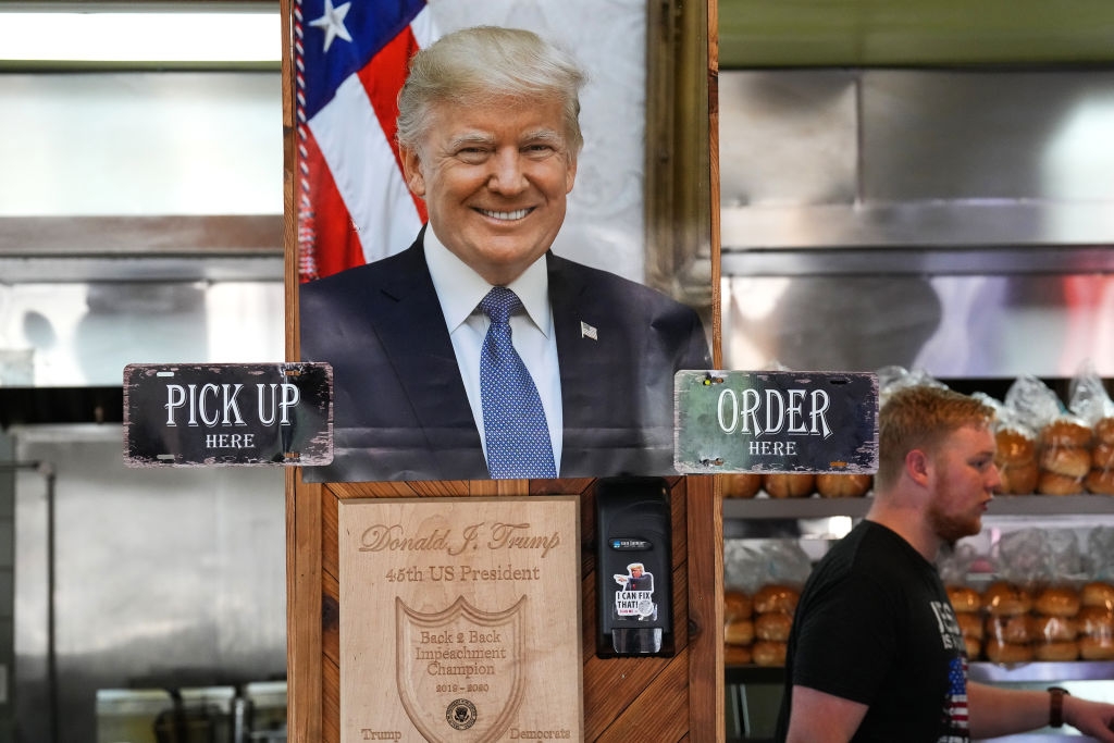 Cutout of a smiling man used as a sign above "Pick Up" and "Order Here" sections in a restaurant. A person walks by in the background