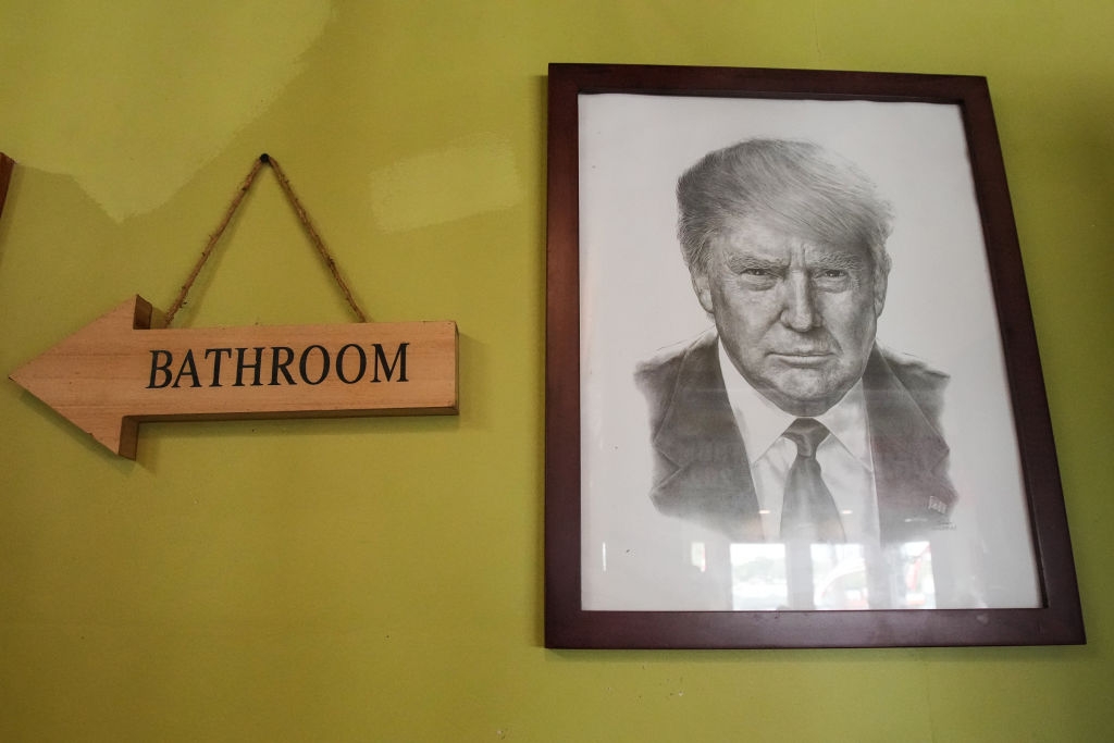 A framed portrait of a serious-looking man beside a wooden arrow sign pointing to a bathroom. The setting appears casual or humorous