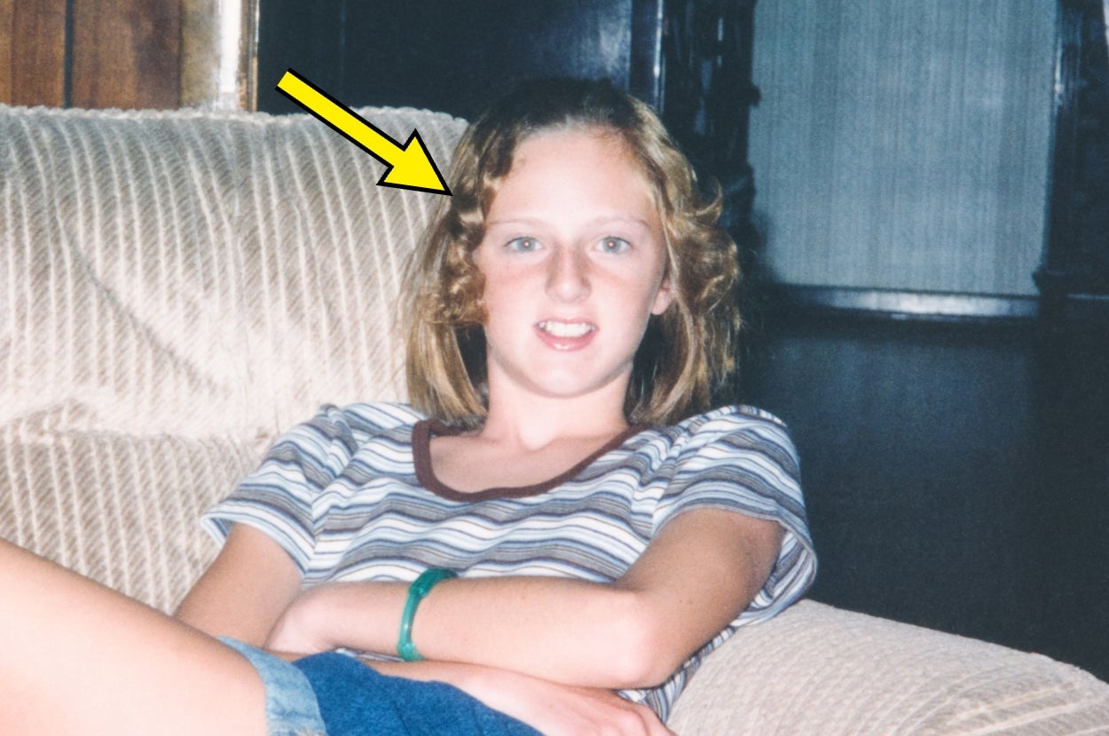 Young person with wavy hair sitting on a couch, wearing a striped shirt and bracelet. Yellow arrow points at their head