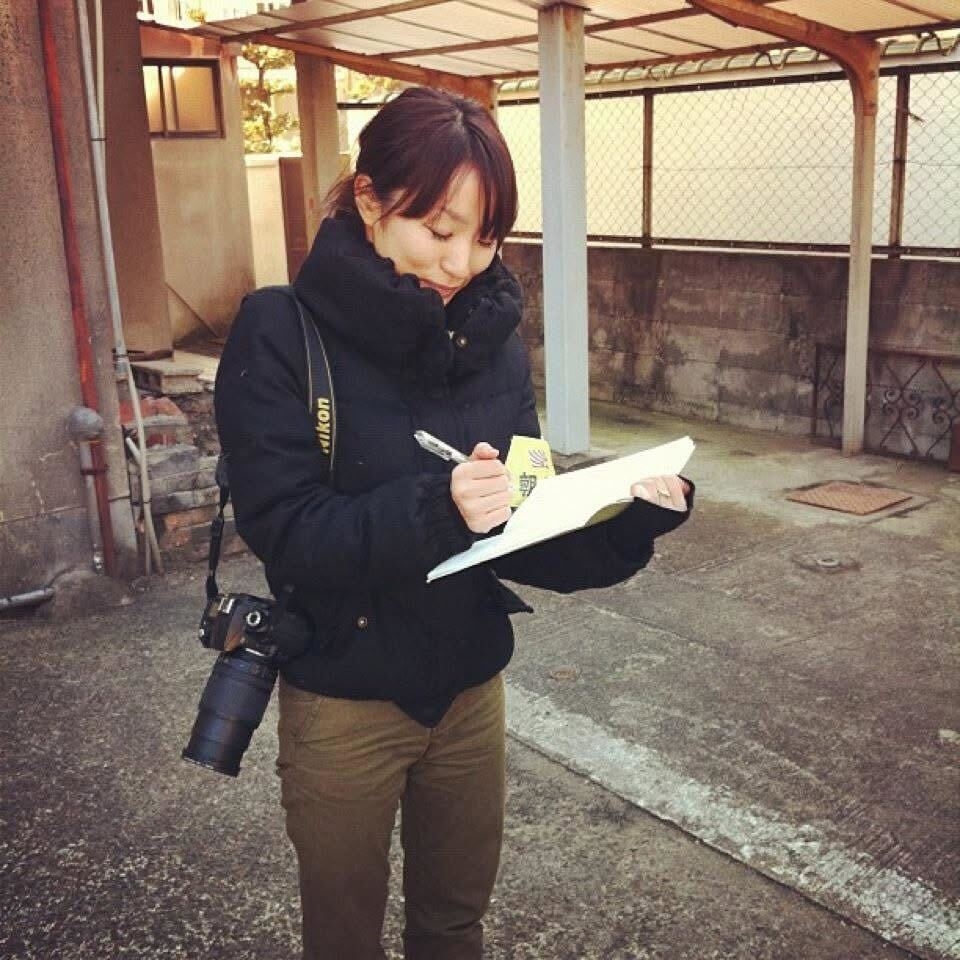 女性が、カメラを身につけて屋外でメモを取っているシーン。カジュアルな服装。