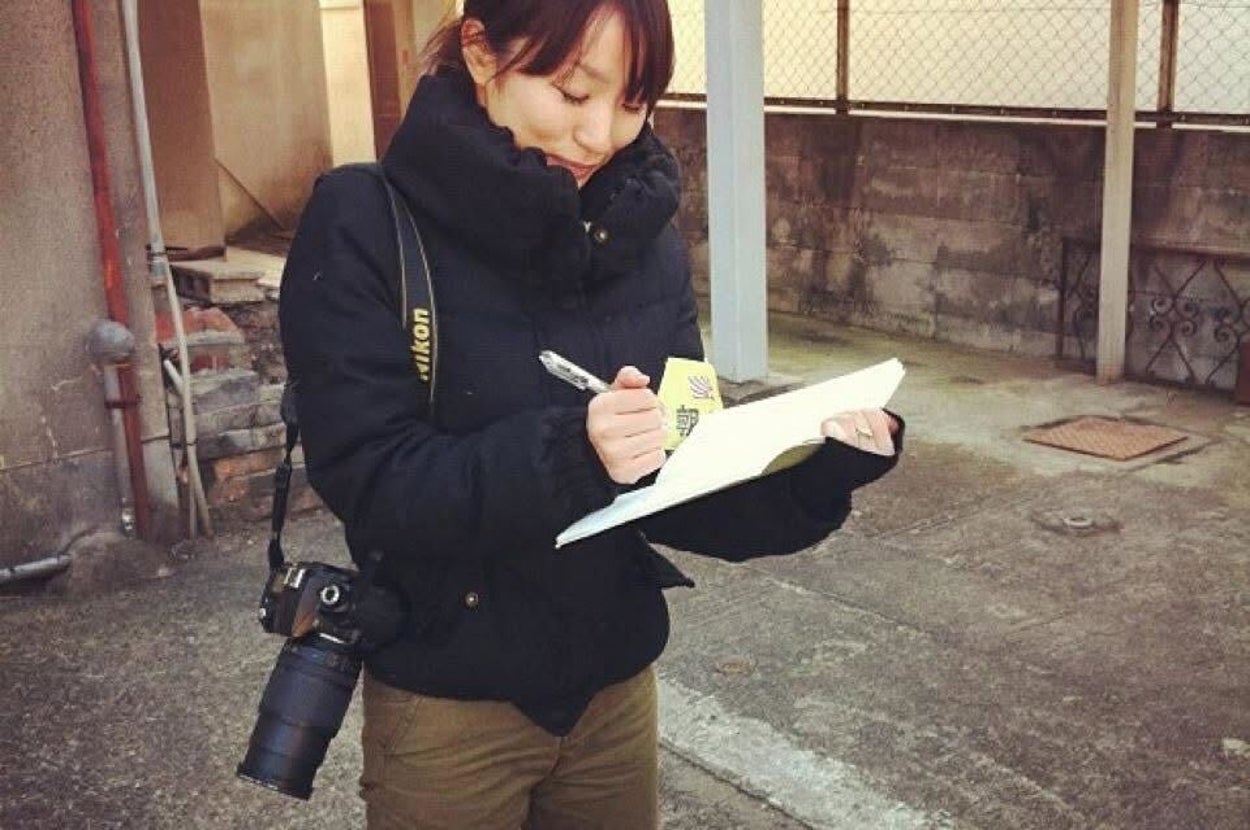女性が、カメラを身につけて屋外でメモを取っているシーン。カジュアルな服装。