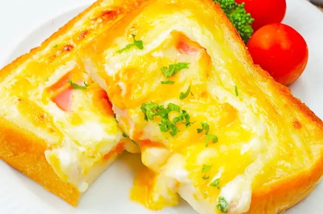 トーストの上にとろけた卵、ハム、卵、パセリ、ブロッコリーとトマト添えた豪華朝食プレート。