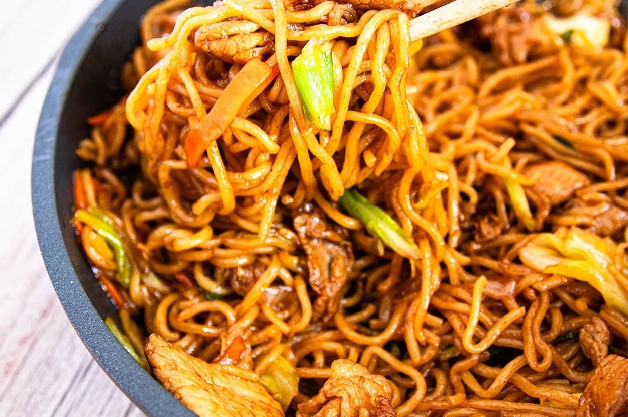 中華鍋で調理された焼きそば。肉と野菜が混ざり、箸で持ち上げられている。