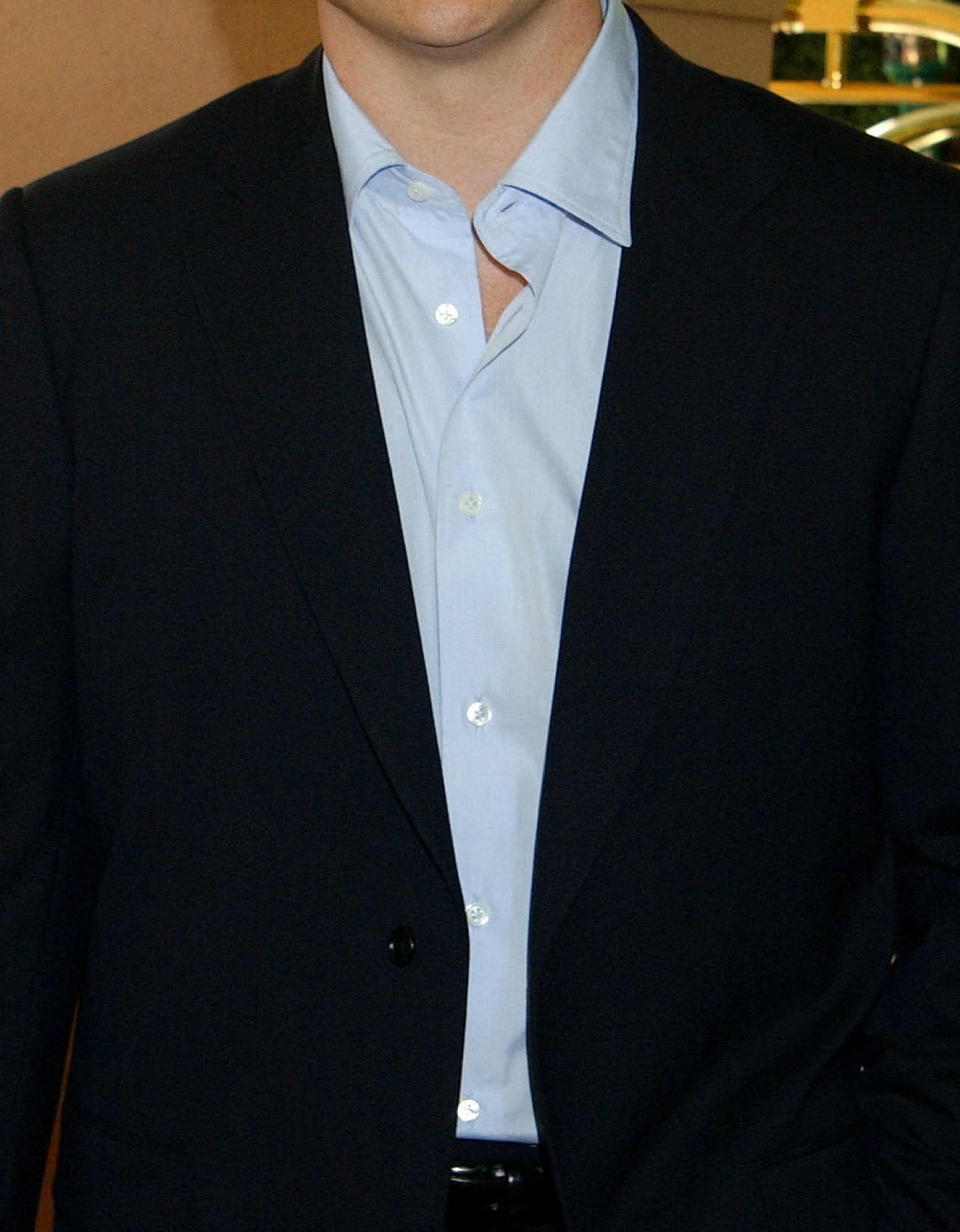 Brendan Fraser in a black suit and light blue shirt on a red carpet, standing in a semi-formal pose