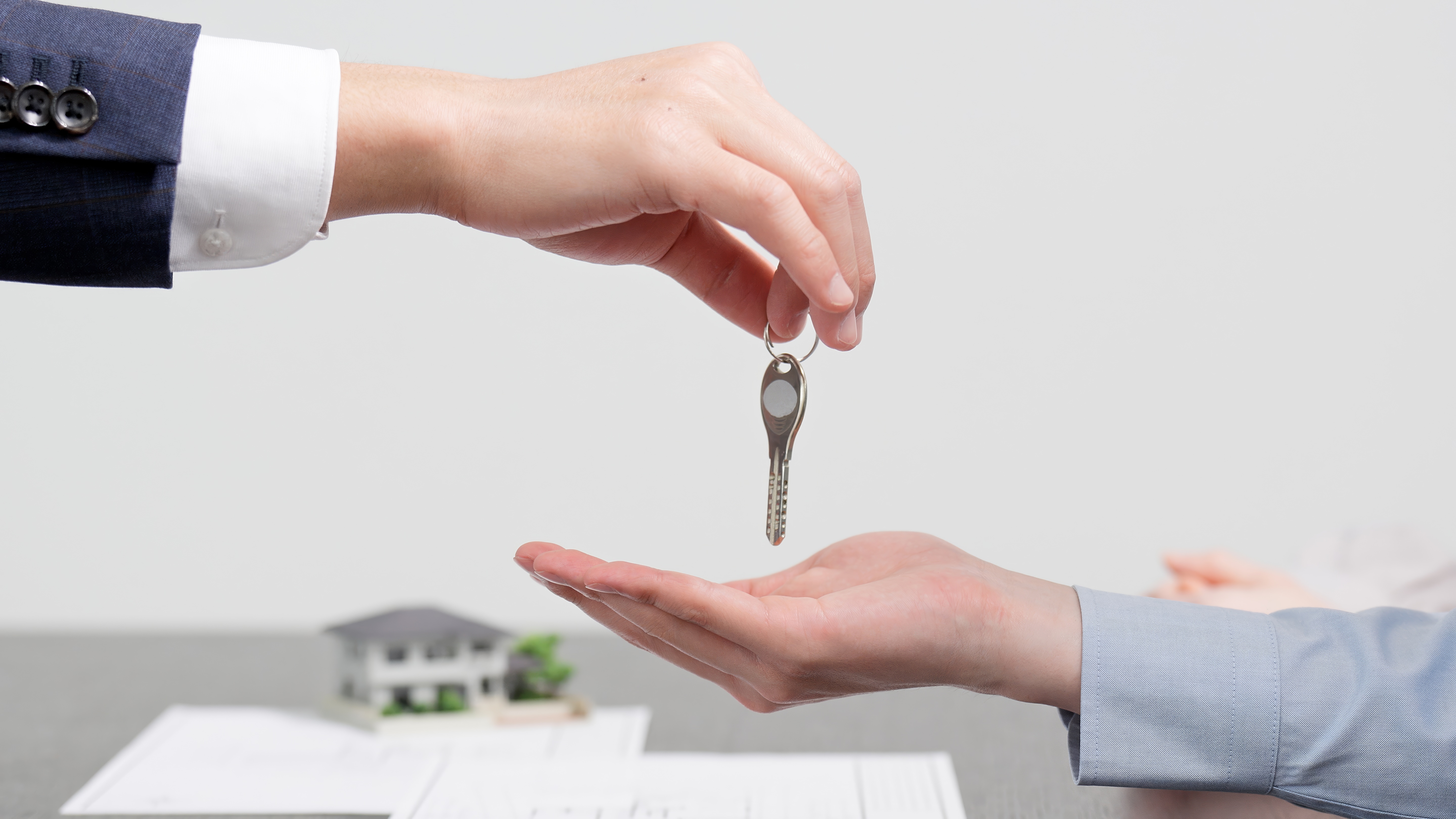 手から手へ鍵を渡す場面。テーブル上には小さな家の模型が置かれている。