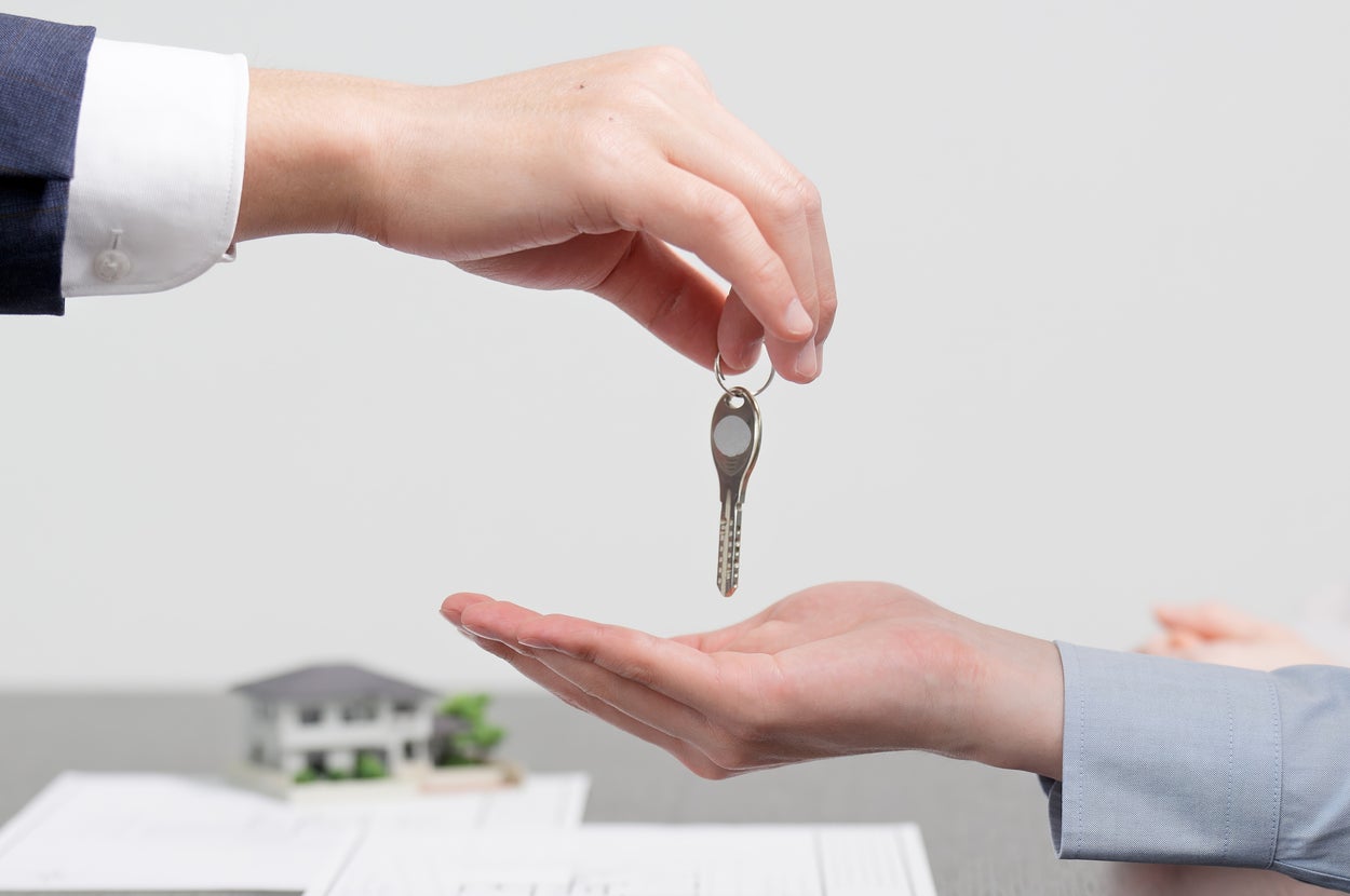 手から手へ鍵を渡す場面。テーブル上には小さな家の模型が置かれている。