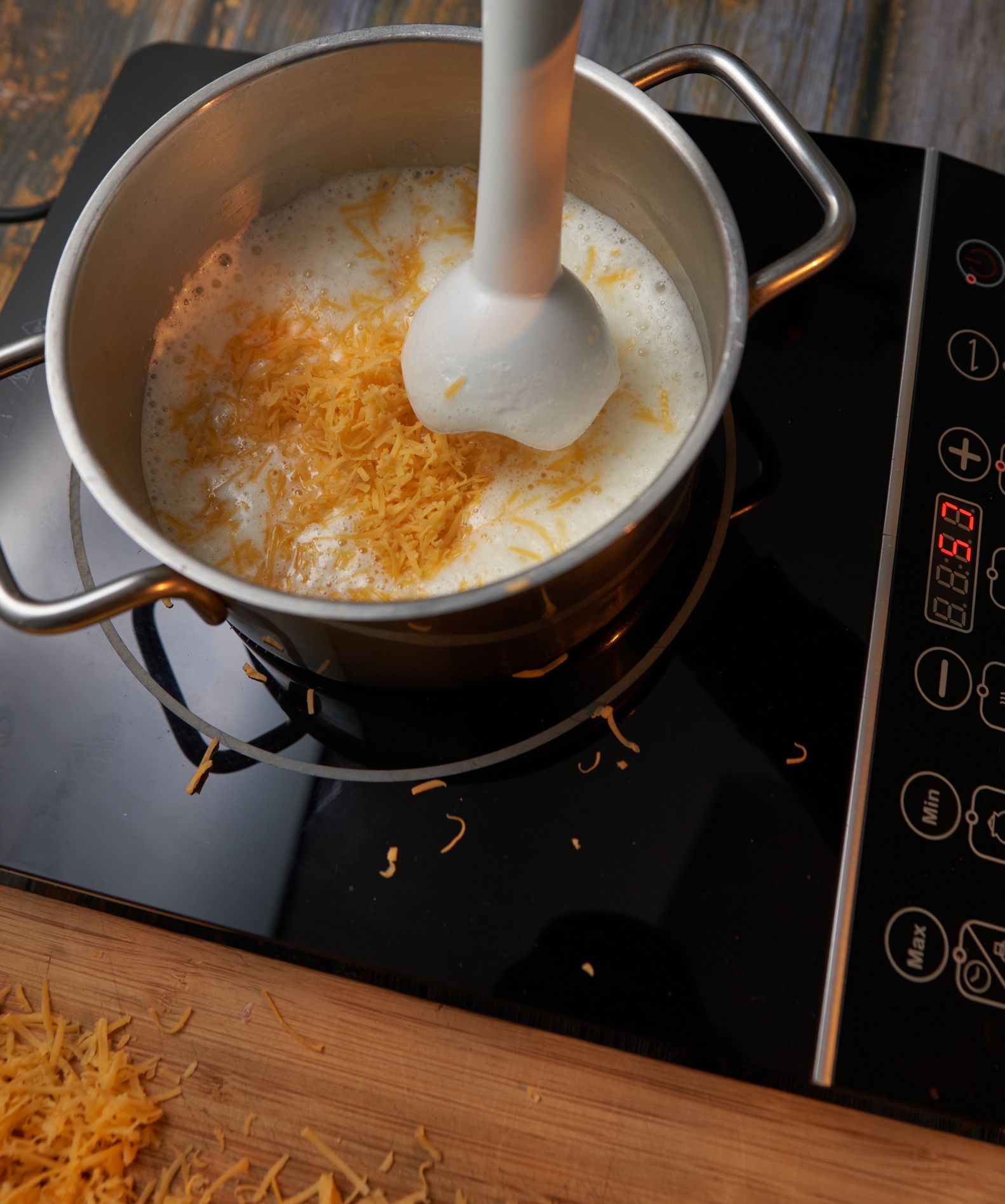 Cheese being blended into a creamy substance  successful  a saucepan connected  an induction cooktop. Some shredded food  is scattered around