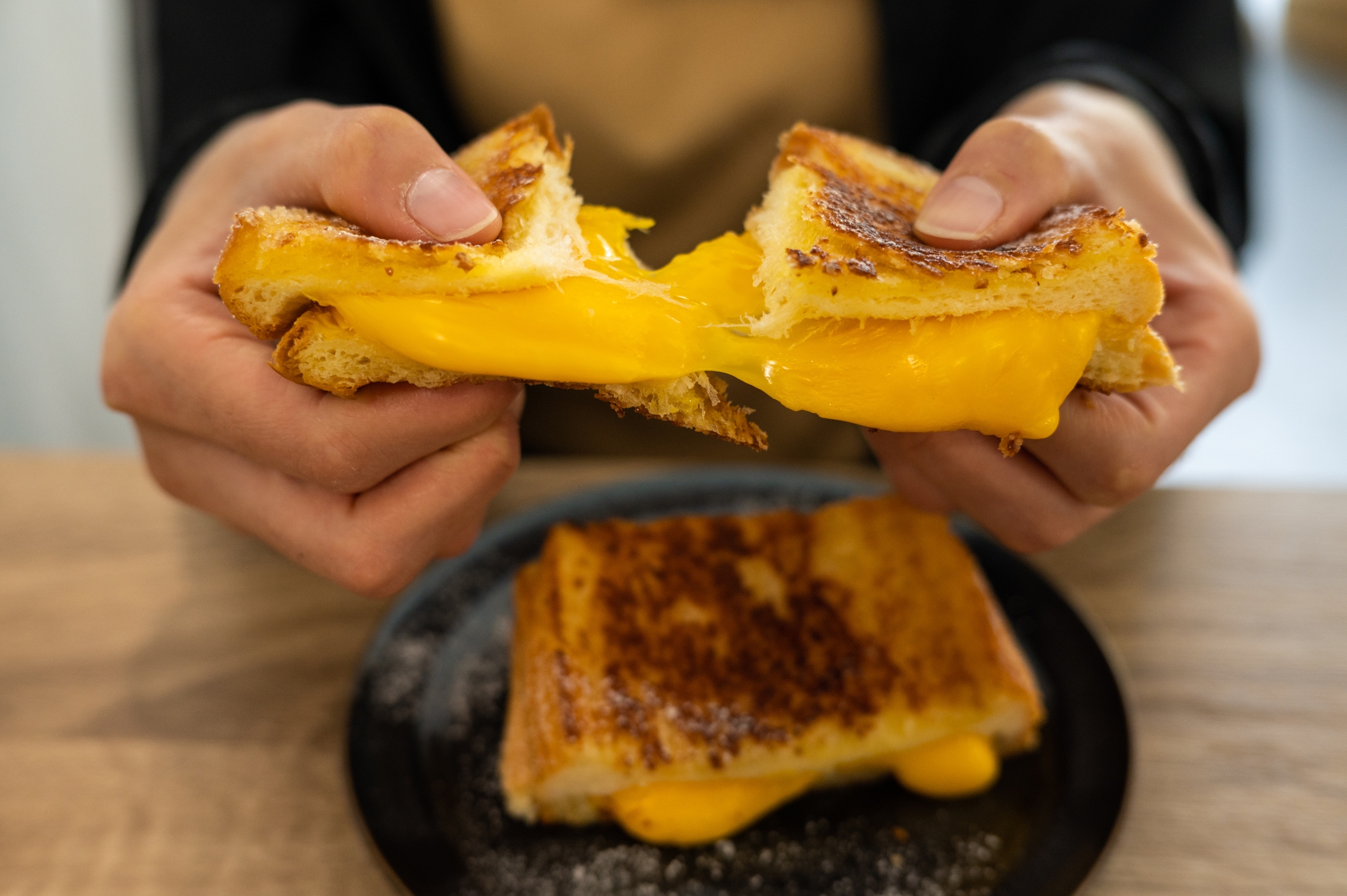 Person pulling isolated  a grilled food  sandwich, with melted food  stretching betwixt  the toasted breadstuff  slices. Another sandwich sits connected  a sheet  below