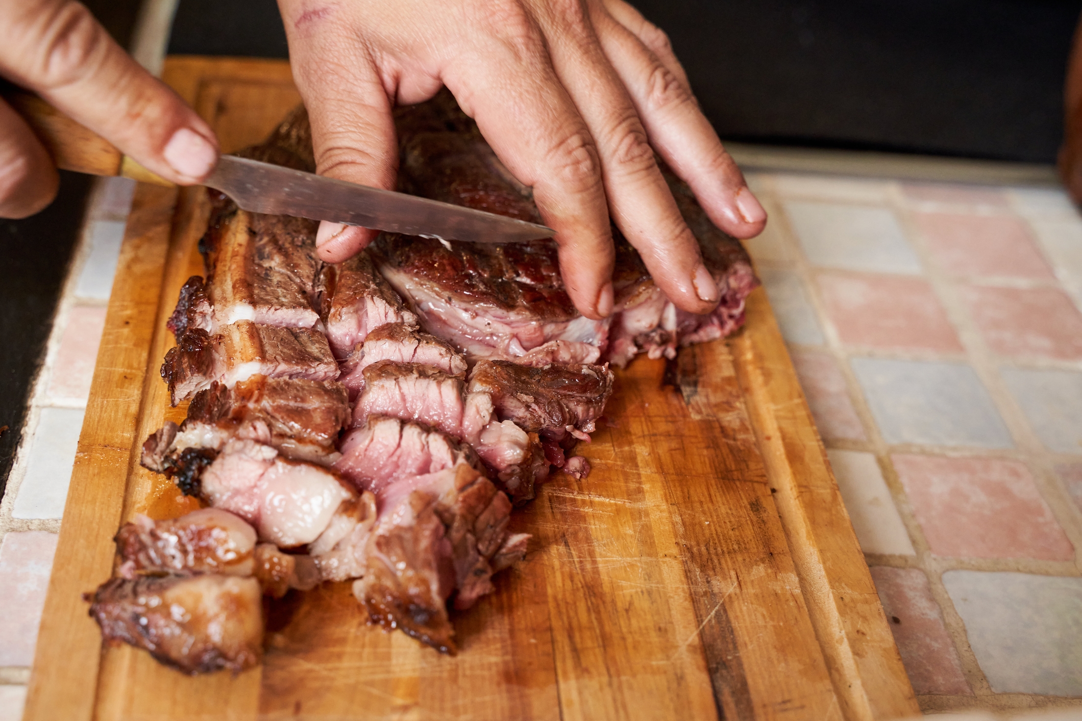 Hands slicing cooked steak connected  a woody  cutting board, showing juicy, tender slices