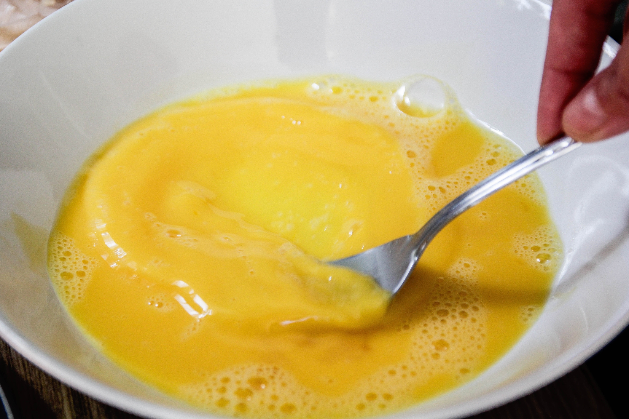 A idiosyncratic   is whisking eggs successful  a achromatic  vessel  with a fork. The eggs are partially mixed with disposable   liquid and bubbles