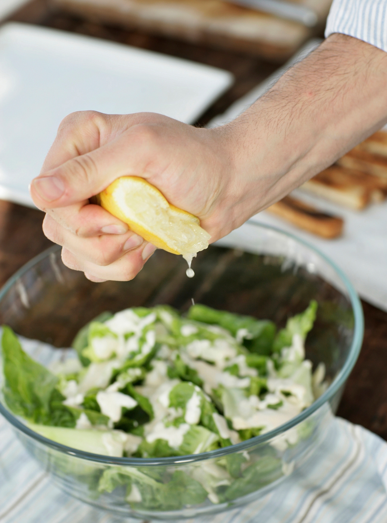 A manus  squeezes a citrus  implicit    a vessel  of crockery   with lettuce and creamy dressing connected  a table