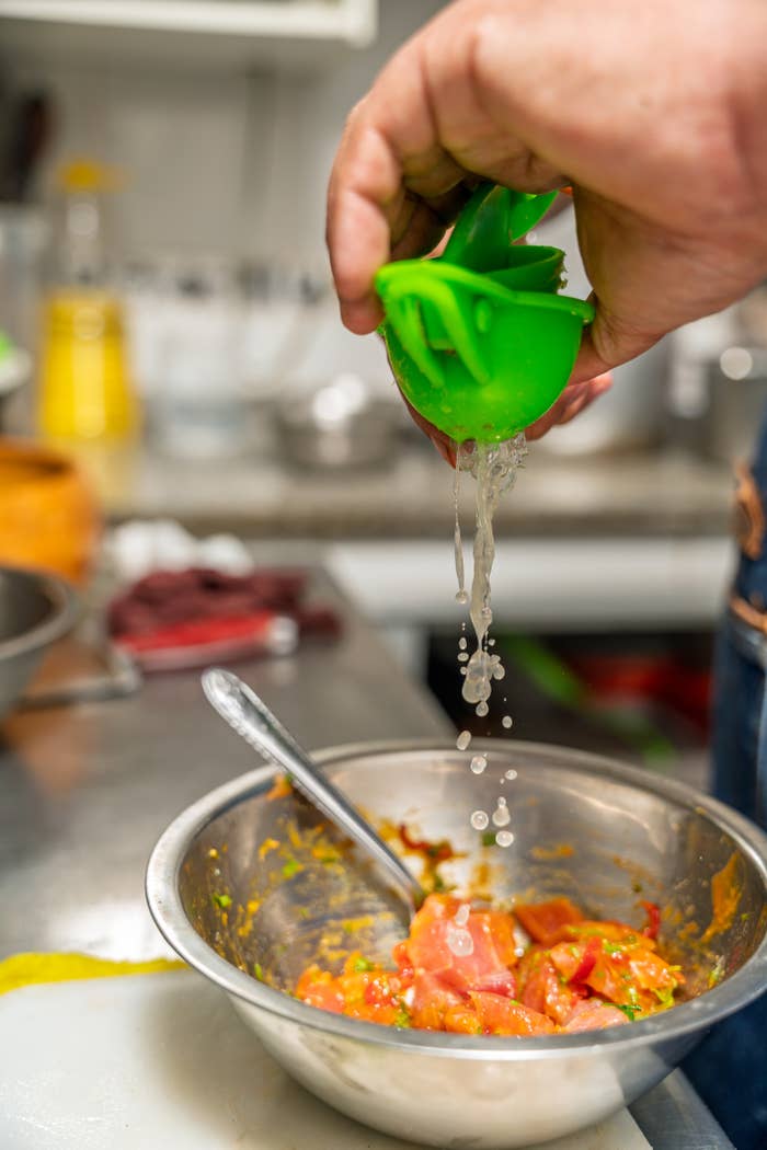 Person squeezing lime foodstuff  into a vessel  of chopped tomatoes and herbs successful  a room  setting