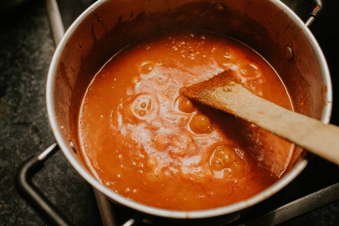 A cookware  of simmering herb  condiment  with a woody  spoon stirring it connected  a stovetop