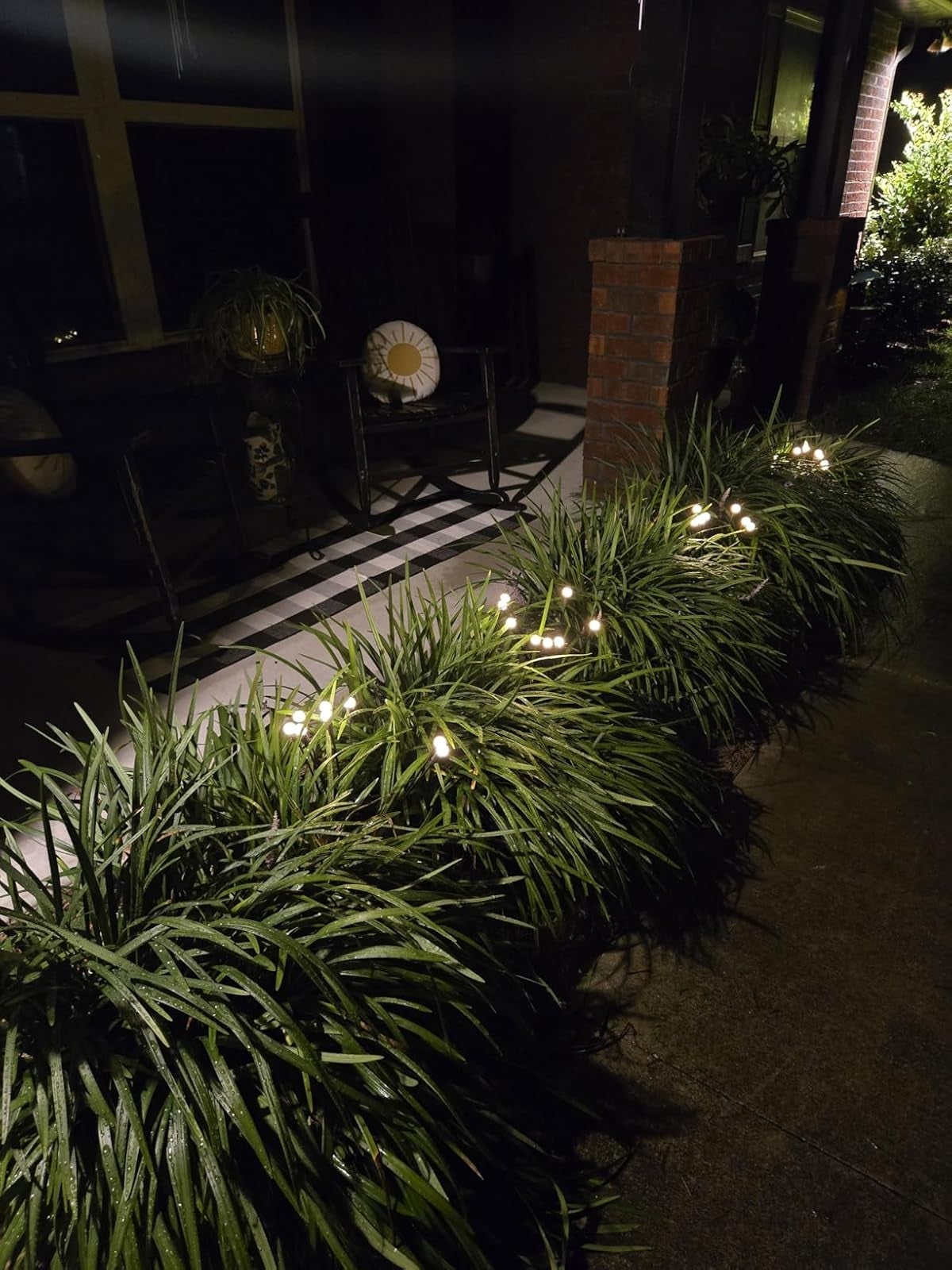 Garden pathway lit by drawstring  lights, with shrubs lining the edge. Comfortable seating disposable   connected  the porch. Ideal for outdoor ambiance shopping