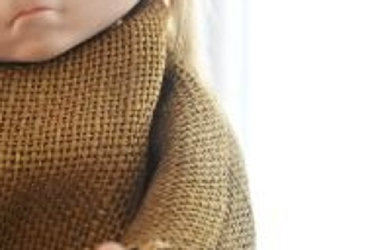 Old doll with large eyes, wearing a tattered dress, displayed in a glass case