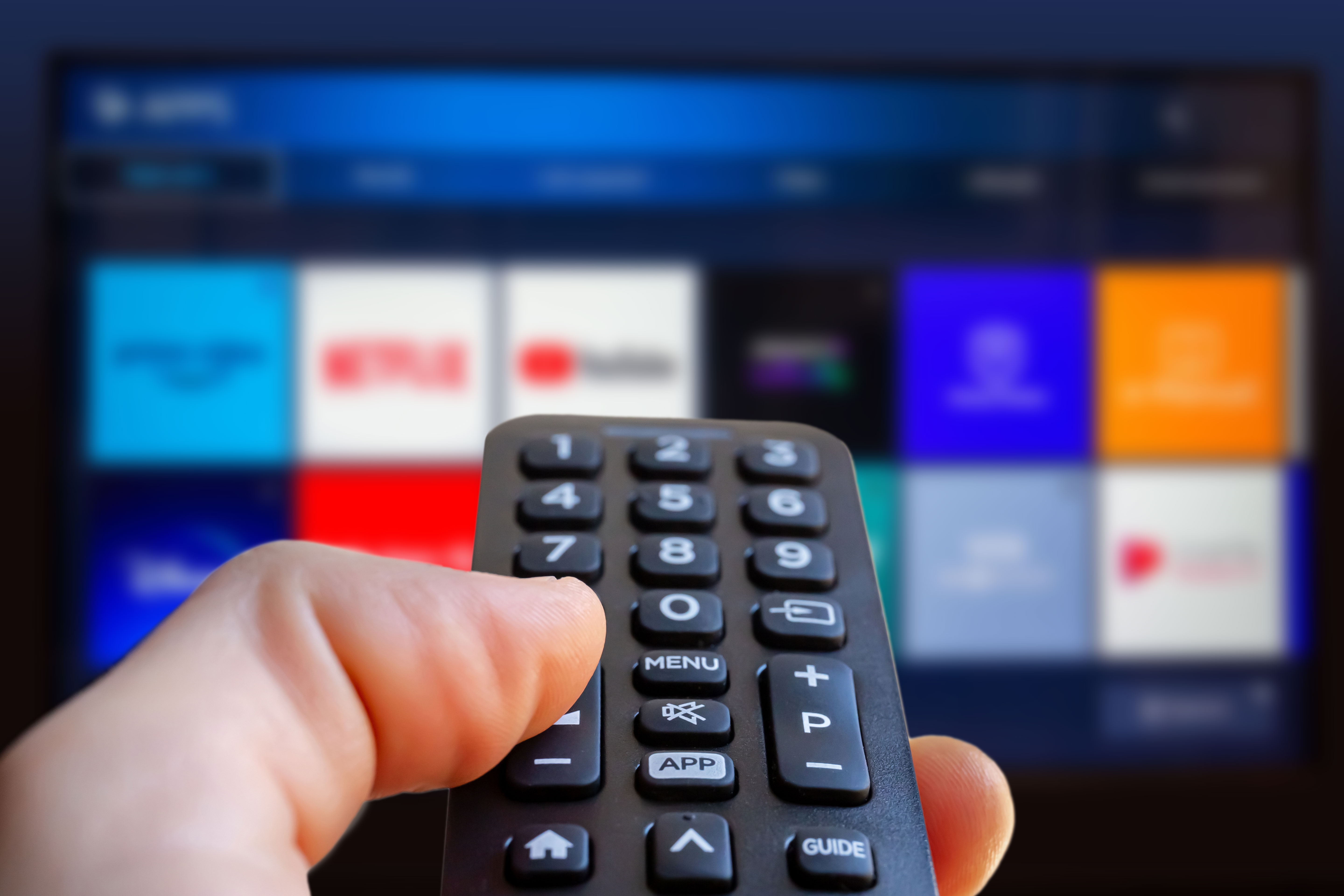 Person utilizing a distant    power  successful  beforehand   of a astute  TV displaying app icons related to streaming services