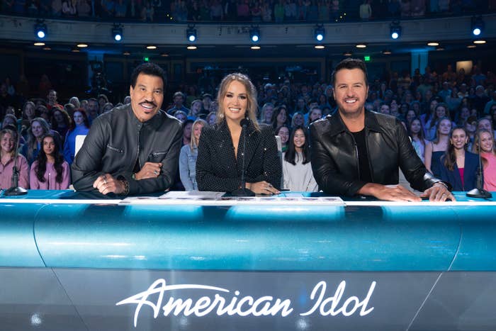 Lionel Richie, Carrie Underwood, and Luke Bryan connected  the "American Idol" panel, smiling and seated astatine  a table  with "American Idol" displayed successful  front