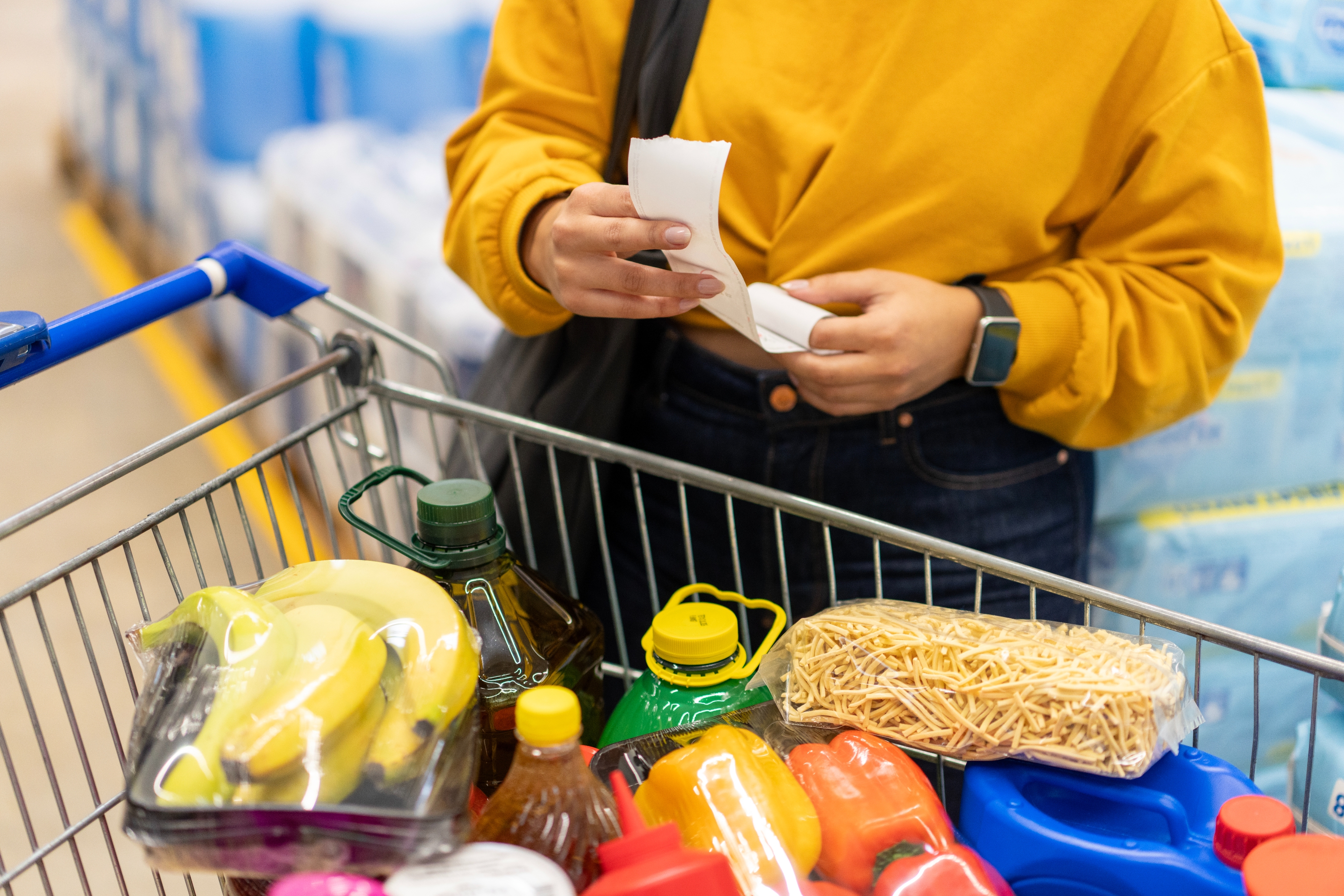 Person checks receipt adjacent   market  cart filled with bananas, oil, noodles, and different   items, suggesting a absorption   connected  buying  and budgeting