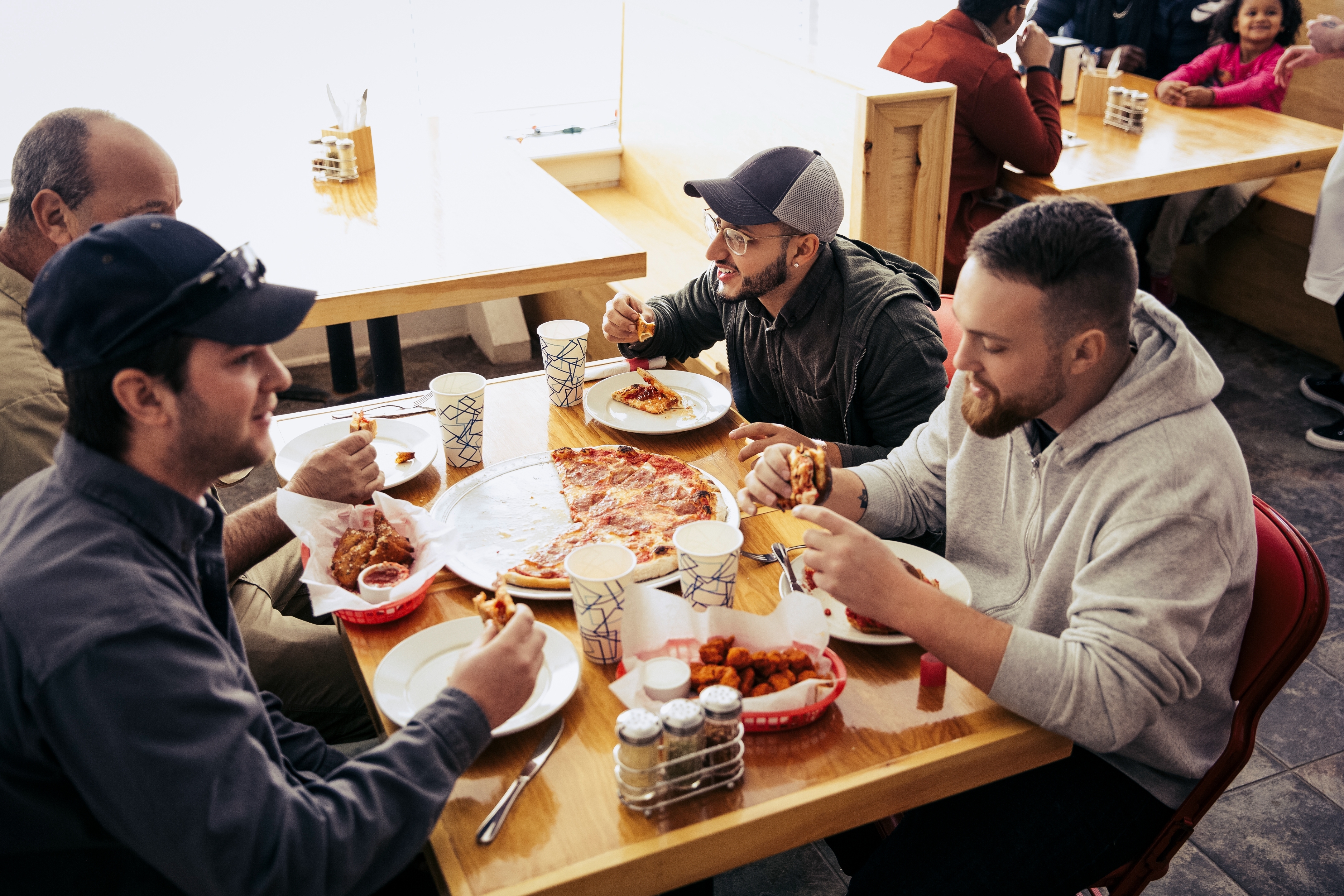 Four radical   casually bask  pizza and wings astatine  a restaurant, engaging successful  conversation