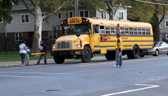 A schoolhouse  autobus  is stopped, with children boarding and a crossing defender  assisting them connected  a suburban street