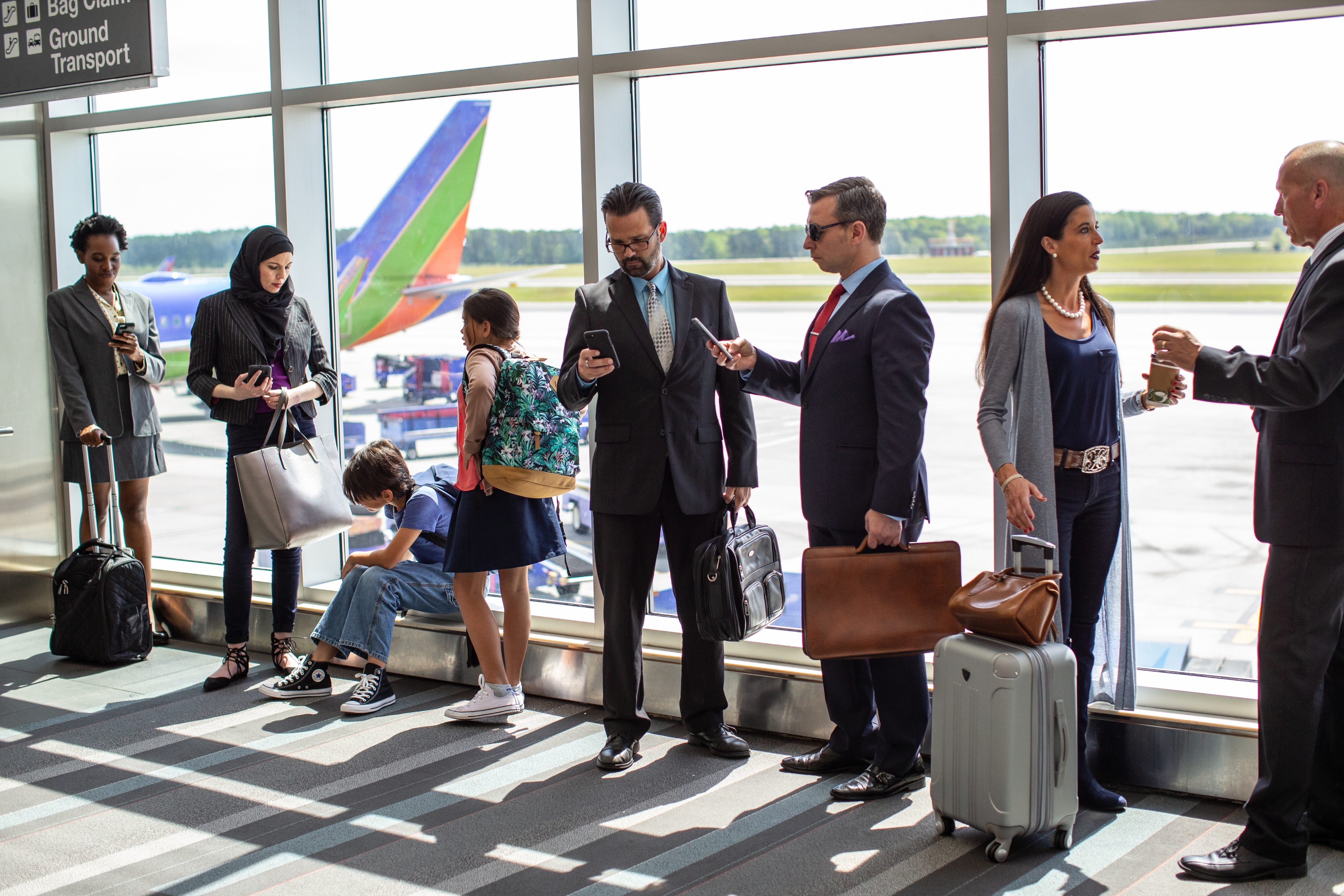 People successful  concern  attire and casual deterioration  basal   successful  an airport. They usage  phones, clasp  luggage, and hold   adjacent   a ample  model   showing a plane