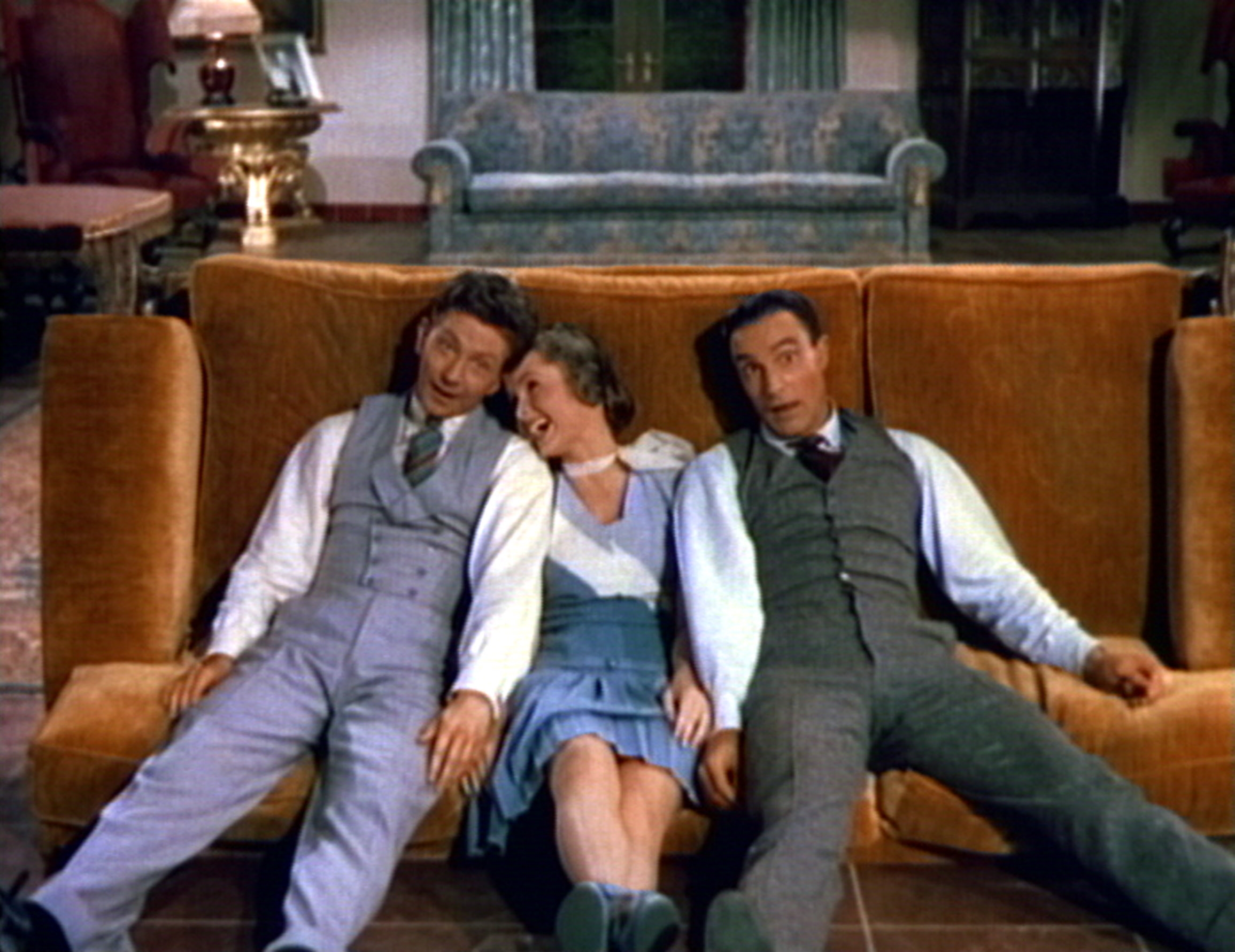Three people in vintage-style suits and dress lounging on a couch, appearing playful and relaxed in a cozy setting