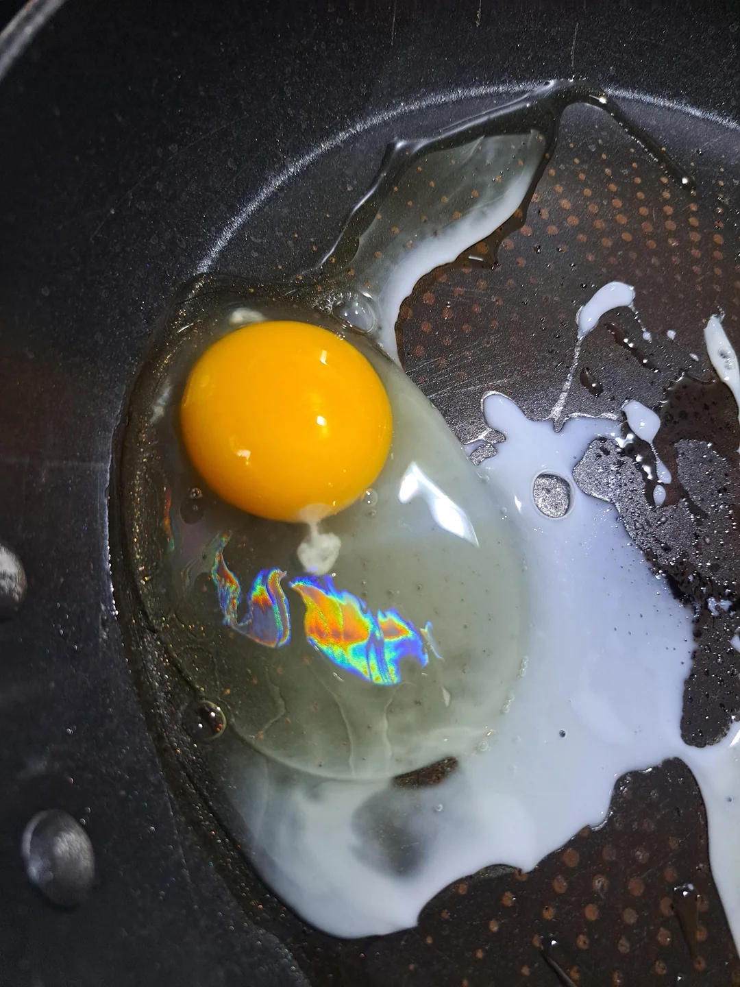 Egg frying successful  a non-stick skillet with oil, showing a rainbow sheen connected  the ovum  whites