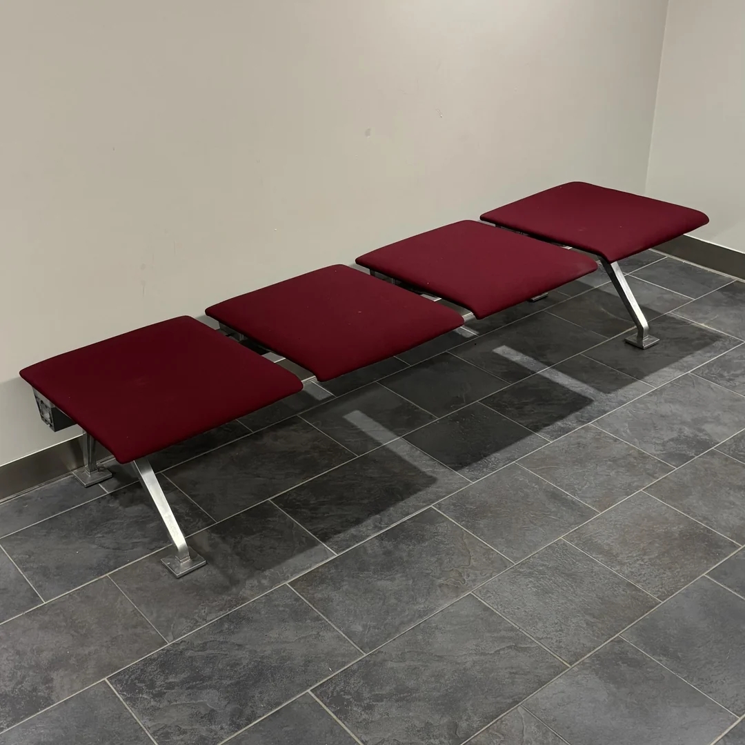 Bench with 4  maroon cushioned seats connected  a tiled level  against a plain wall