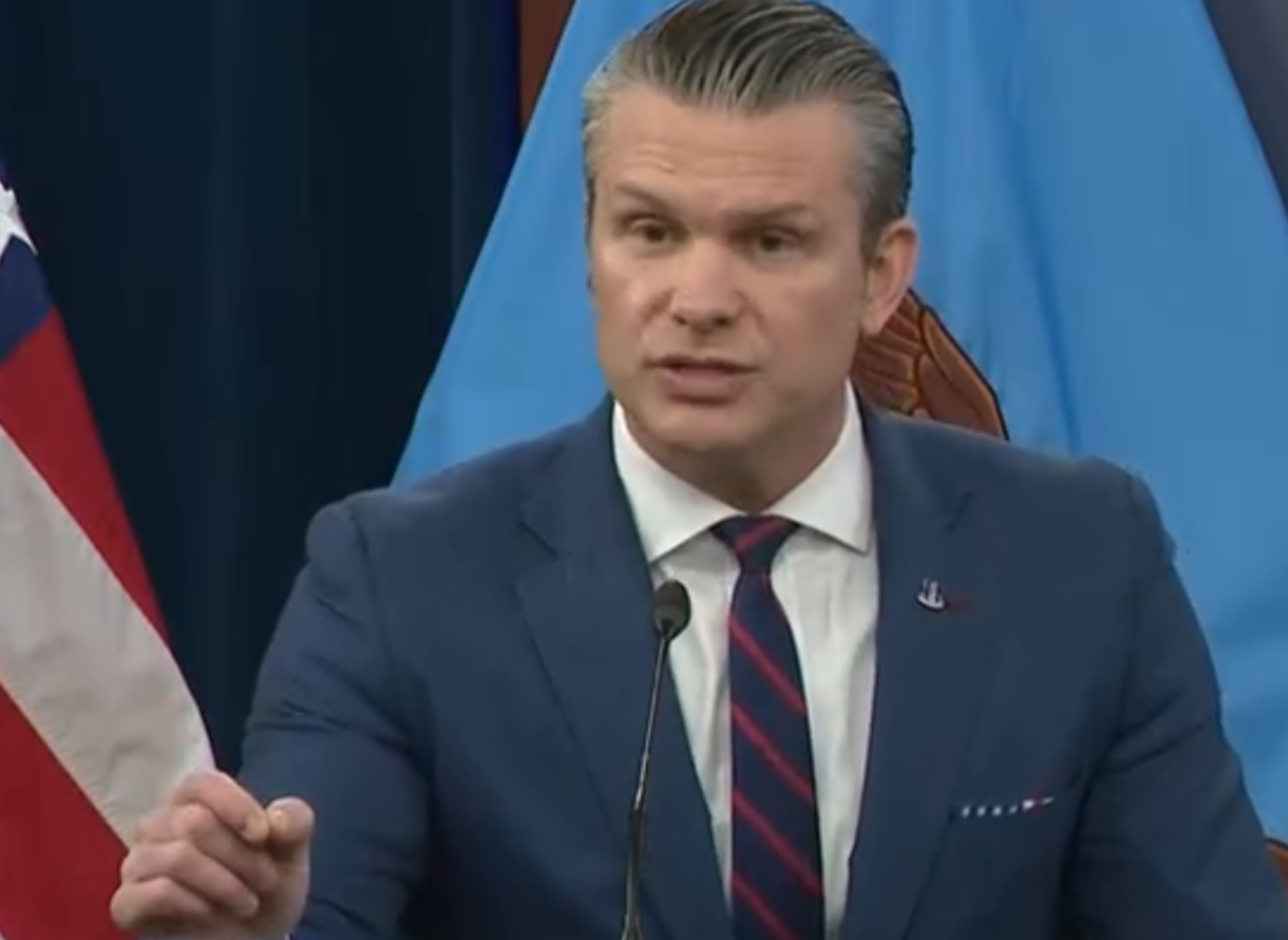 Man successful  a suit   speaks astatine  a podium with flags successful  the inheritance  during a quality    conference