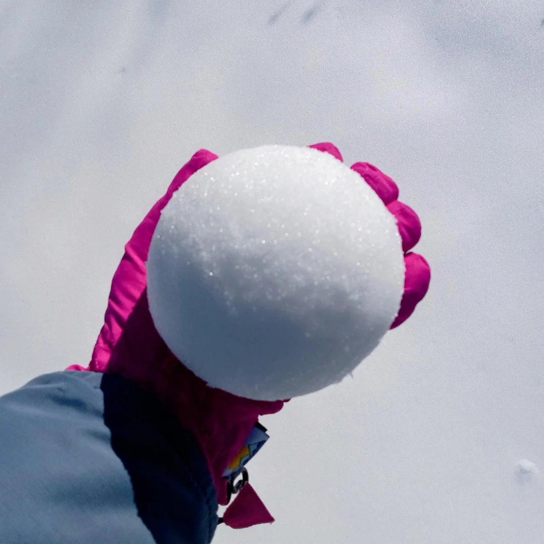 Person successful  a wintertime  overgarment  holding a snowball successful  their gloved manus  against a snowy background