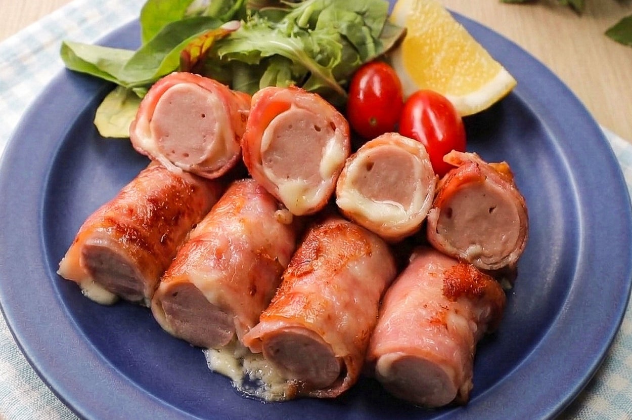 ベーコンで巻かれたソーセージが青い皿に盛られ、レタスやトマト、レモンが添えられている料理。