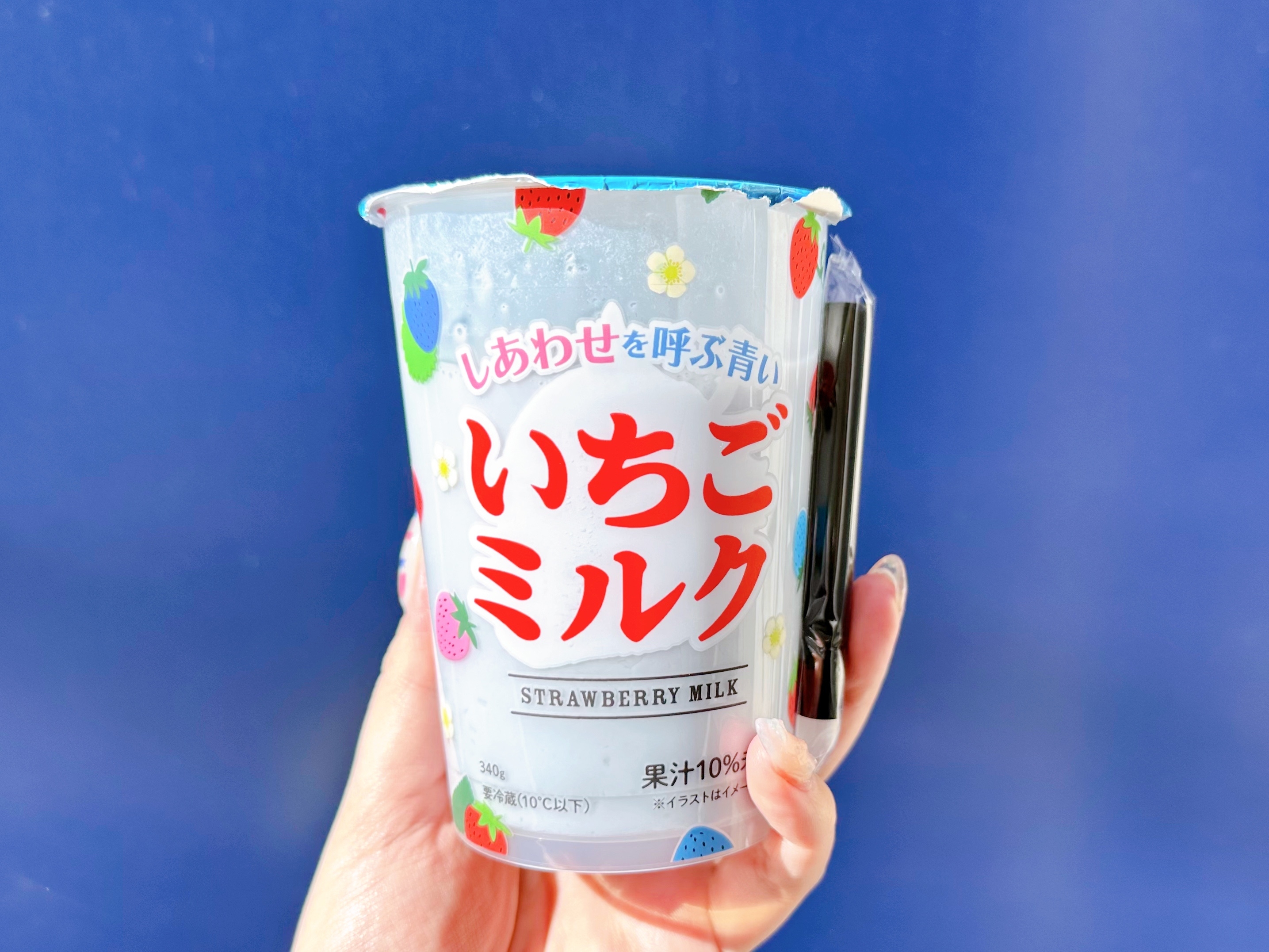 手に持たれた「いちごミルク」のカップ、ストロベリーイラストが散りばめられています。
