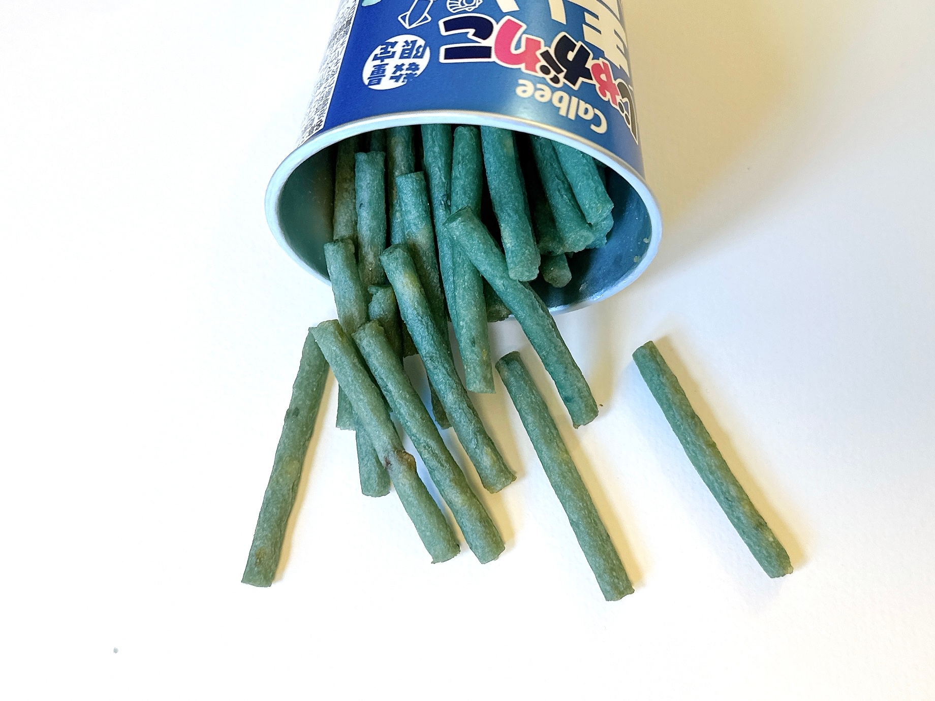 スナック菓子の入った筒が横になり、中から緑色のスティック状のスナックがこぼれています。