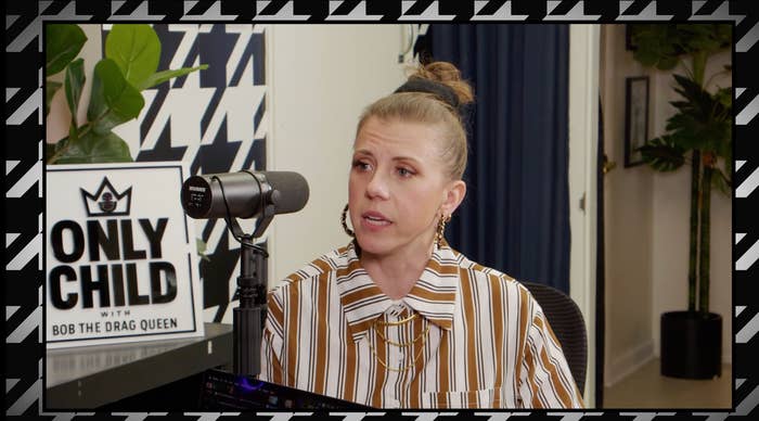 Person successful  a striped garment  speaking into a microphone connected  a podcast. Sign reads "Only Child with Bob the Drag Queen." Indoor mounting  with plants