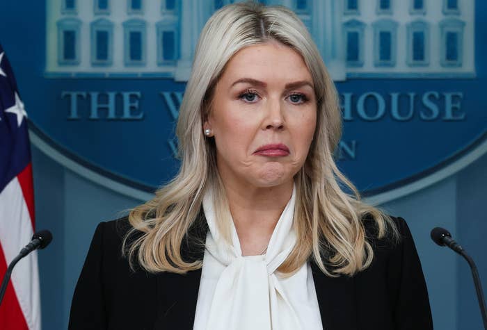 A person stands at a podium with "The White House" background, wearing a black blazer and white blouse, appearing to make a statement