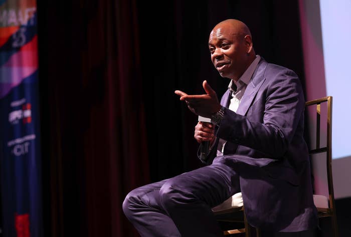 Comedian sitting connected  signifier    successful  a suit, speaking animatedly into a microphone astatine  a unrecorded  event