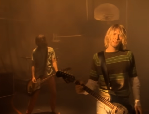 Two musicians execute  connected  signifier    with guitars. The foreground instrumentalist  wears a striped sweater implicit    a long-sleeve shirt. Basketball hoops are disposable   above
