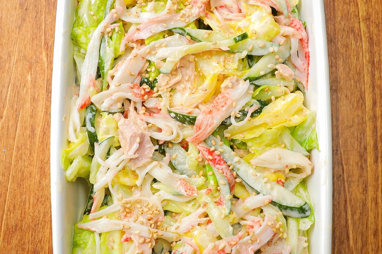 たっぷりのカニカマやレタス、きゅうりが入ったサラダが白い皿に盛り付けられています。健康的で鮮やかな料理です。