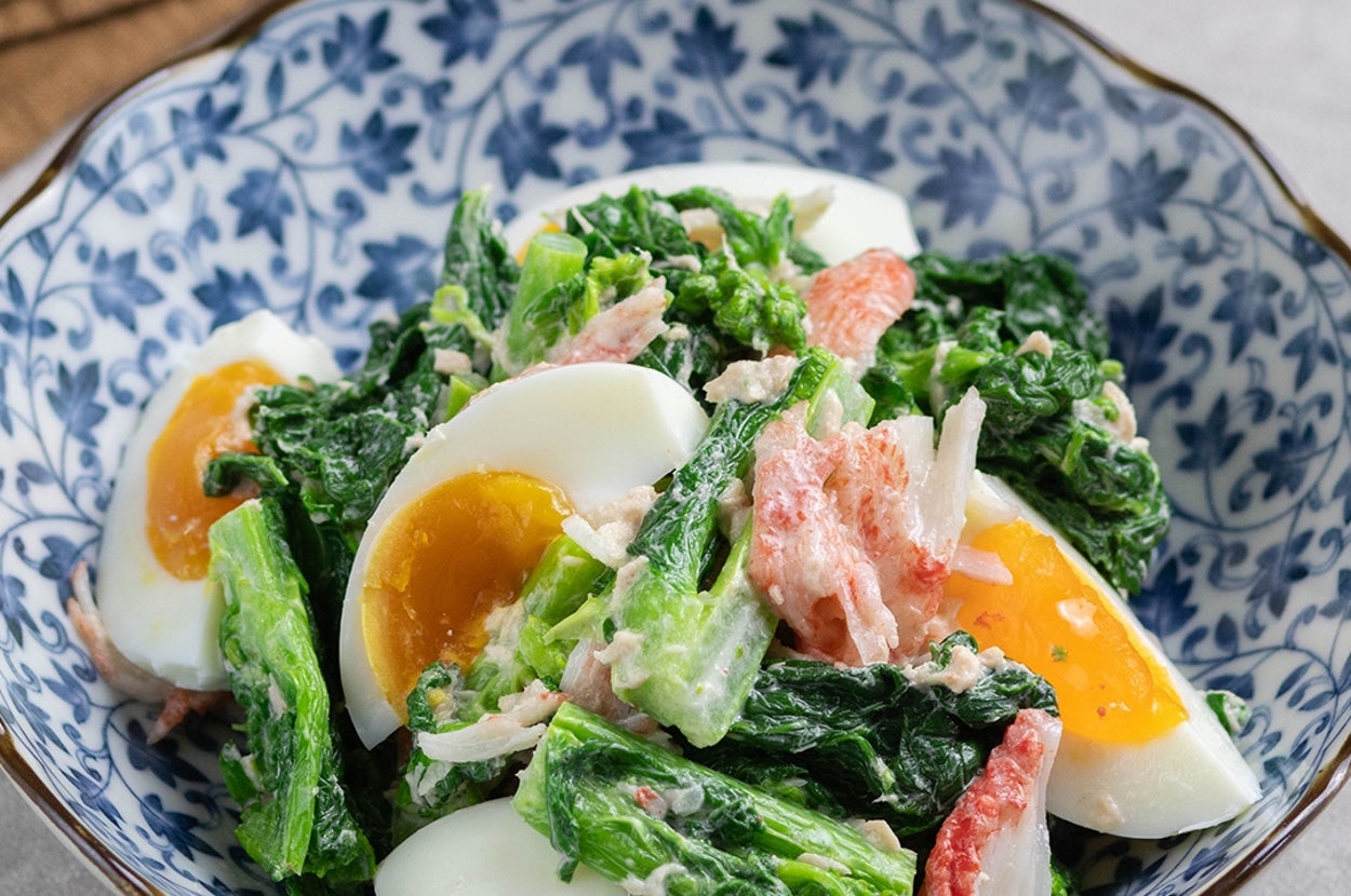 青い模様入りの器に盛られたサラダ。ゆで卵、葉物野菜、カニ風味かまぼことドレッシングが混ぜられている。