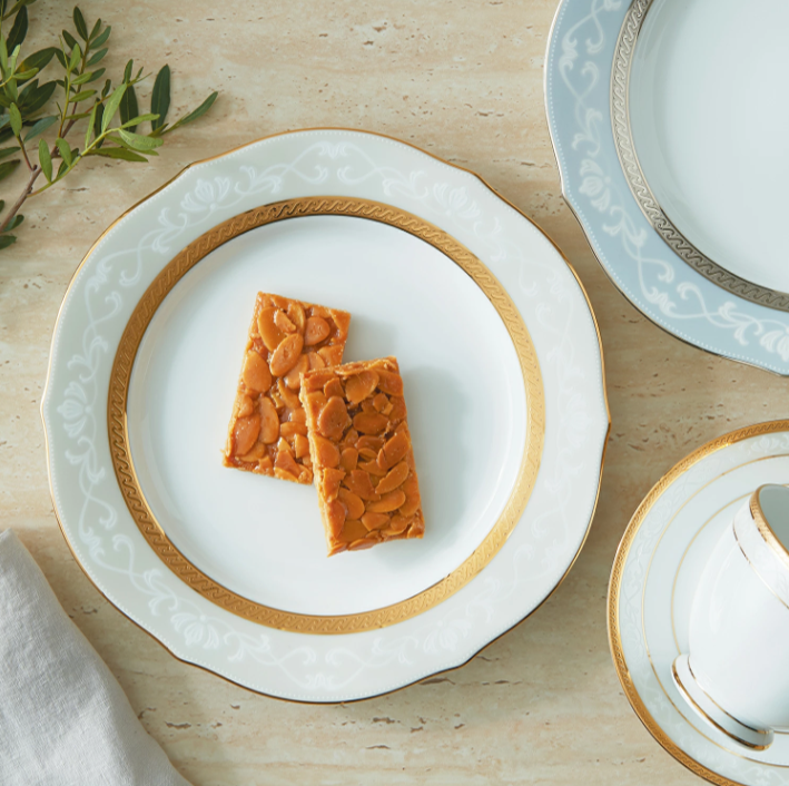 白い高級感のあるプレートにナッツの入った2枚のバーがのせられている。隣にティーカップと植物が飾られている。