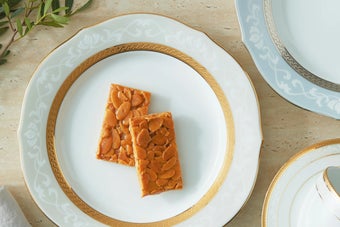 白い高級感のあるプレートにナッツの入った2枚のバーがのせられている。隣にティーカップと植物が飾られている。